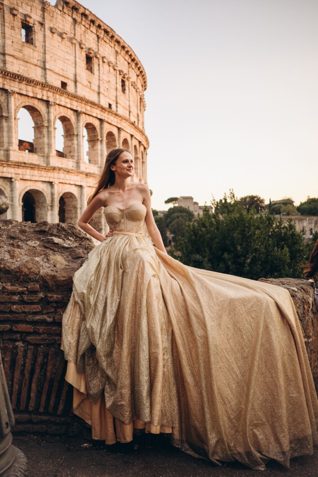 Gold flying dress with its train spread over ancient stones by the Colosseum