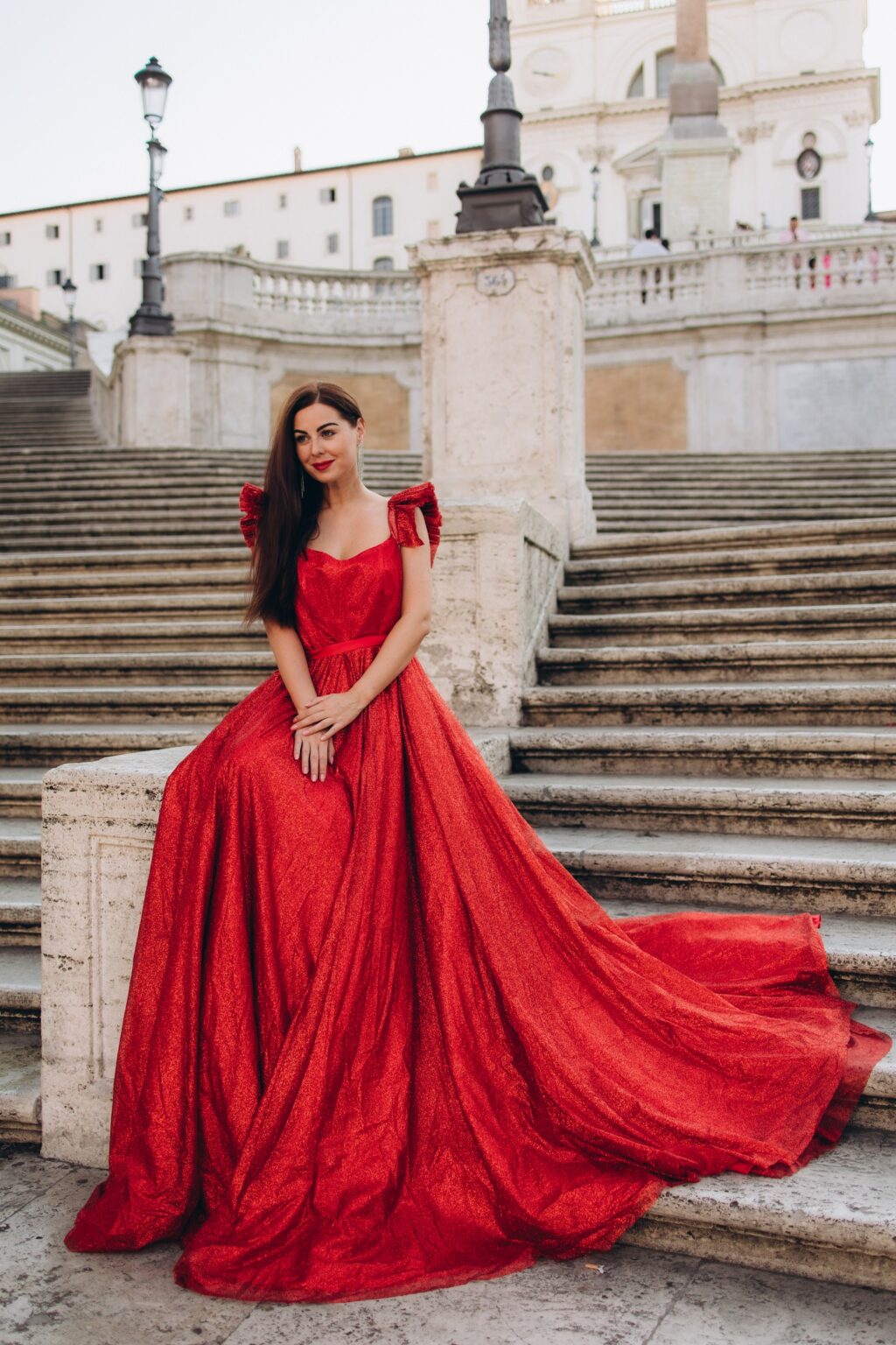 Woman in a red gown sitting on the Spanish Steps, her train spread over the stairs