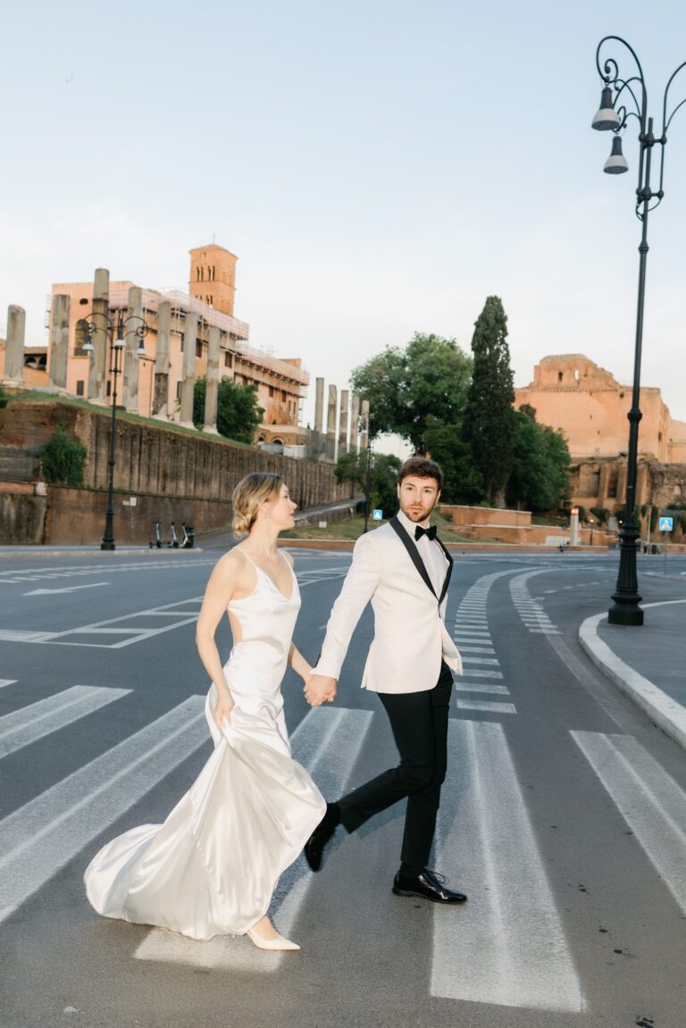 Bride and groom walking across an empty street by the Colosseum at 7:30am