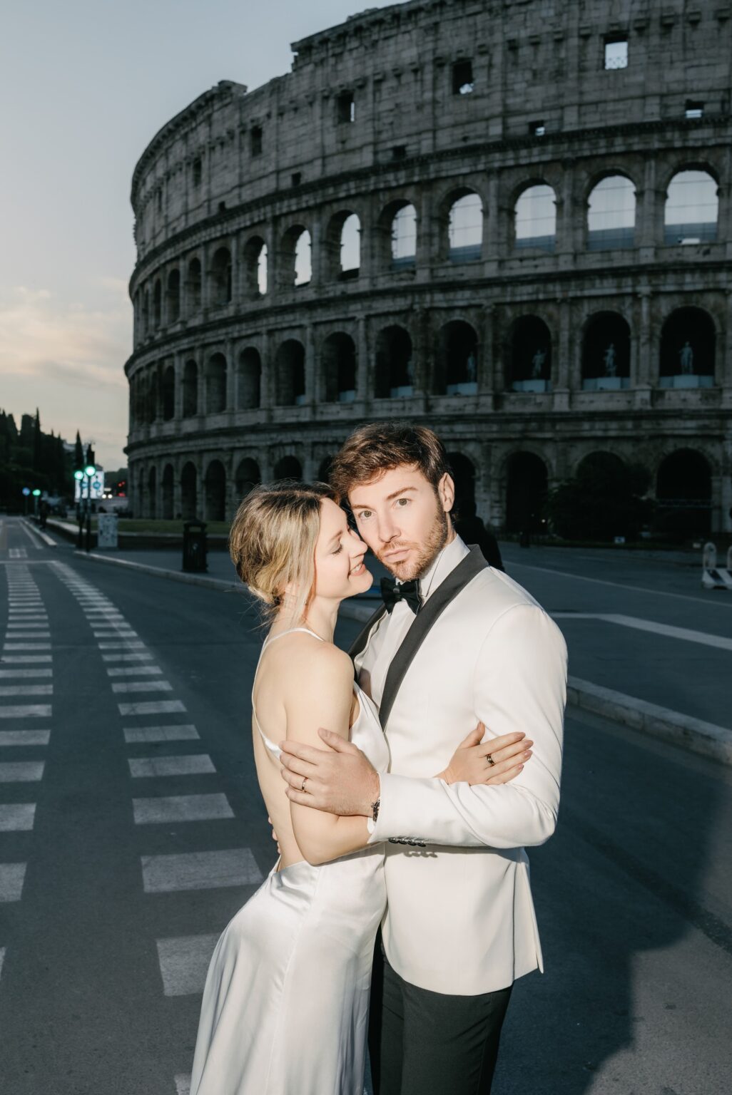 Bride and groom in a white tuxedo and silk dress in front of the Colosseum
