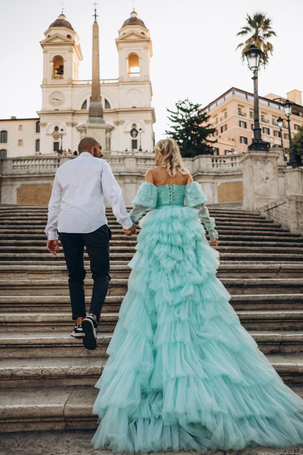 Couple climbing the Spanish Steps towards Trinità dei Monti, her mint tulle train on the stairs